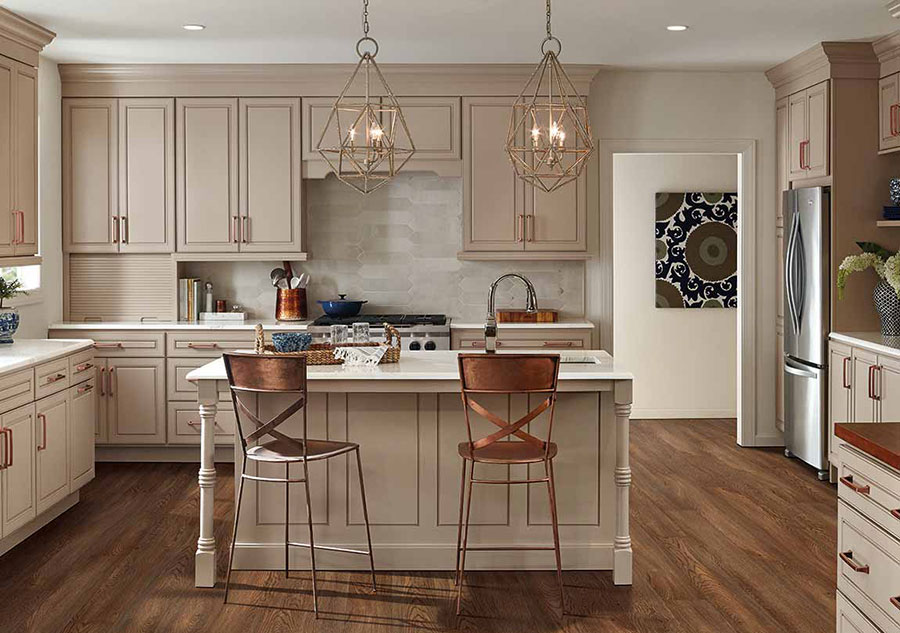 A classic kitchen with island and bar seating with bronze chairs, beige cabinets, and stainless steel appliances.